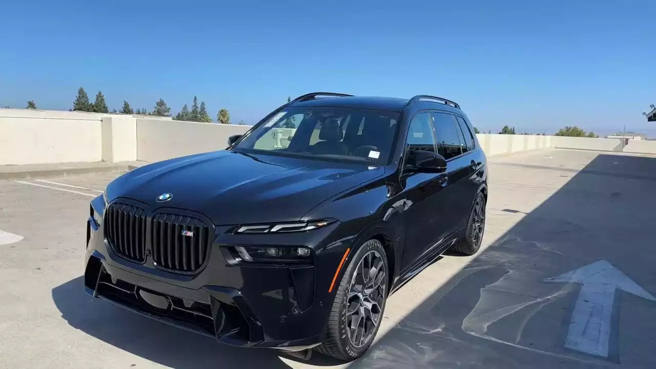 Black BMW SUV parked on a concrete surface with a clear blue sky.