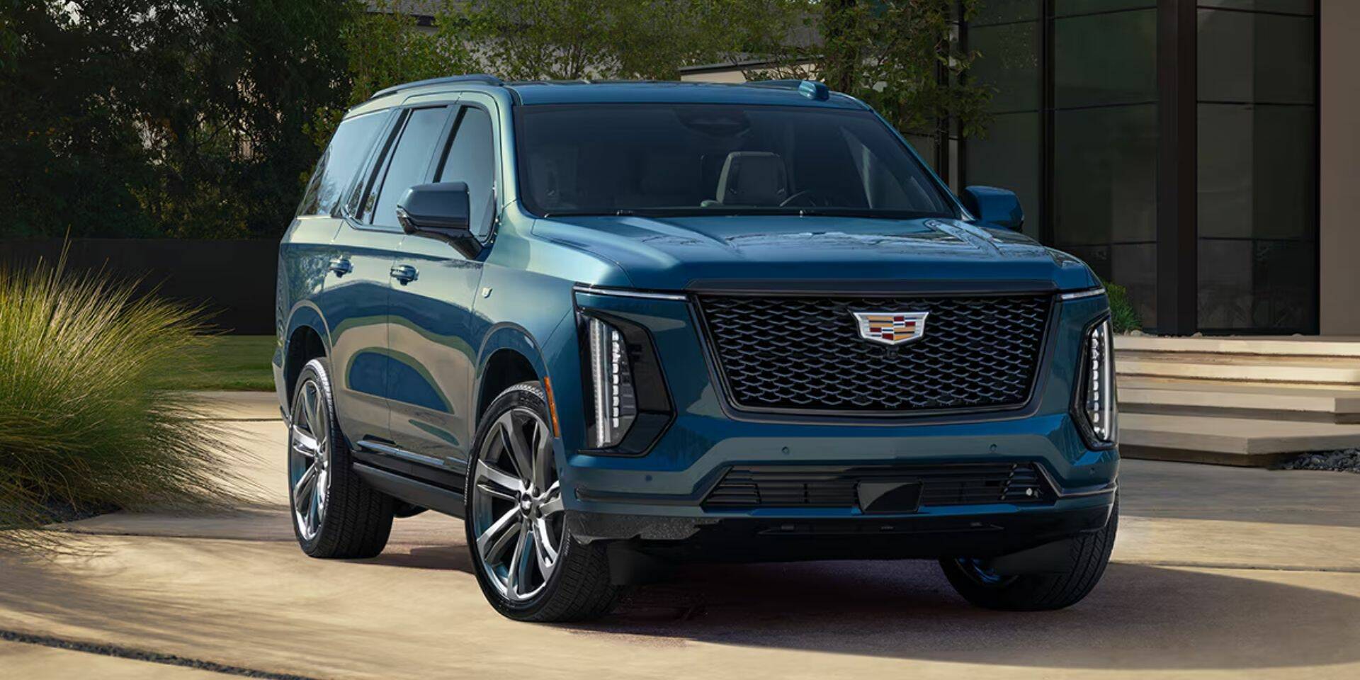 Blue Cadillac SUV parked on a driveway with a modern building in the background