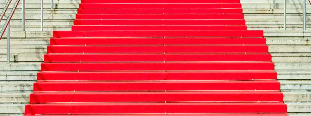 A bright red carpet runner draped up a wide set of outdoor concrete stairs with metal railings on both sides.