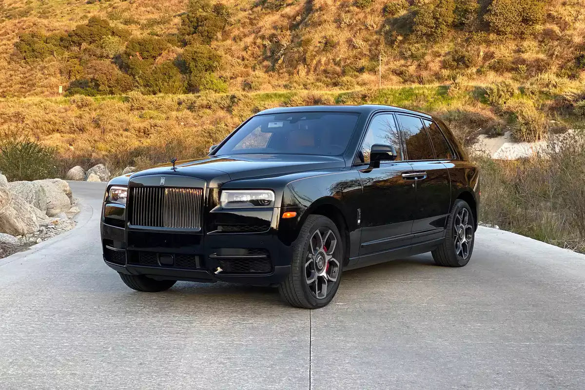 A black Rolls-Royce Culliance SUV parked on a paved road with dry grassy hills in the background.