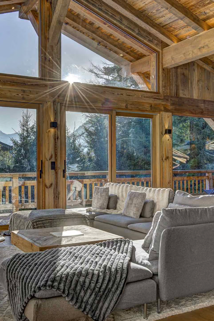 A modern gray sectional sofa in a rustic wooden chalet living room, with a gray knit throw blanket draped over the arm and large windows showing a mountain view.