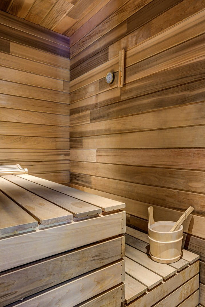 A traditional wooden sauna interior with wooden walls and benches, a small wooden bucket with a wooden spoon, and a steam generator on the right side.
