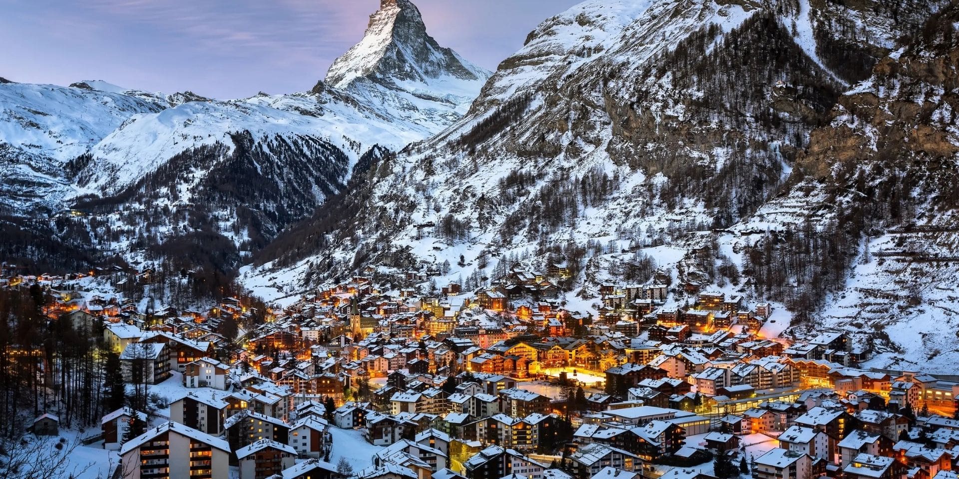 Snowy mountain village with illuminated buildings at dusk