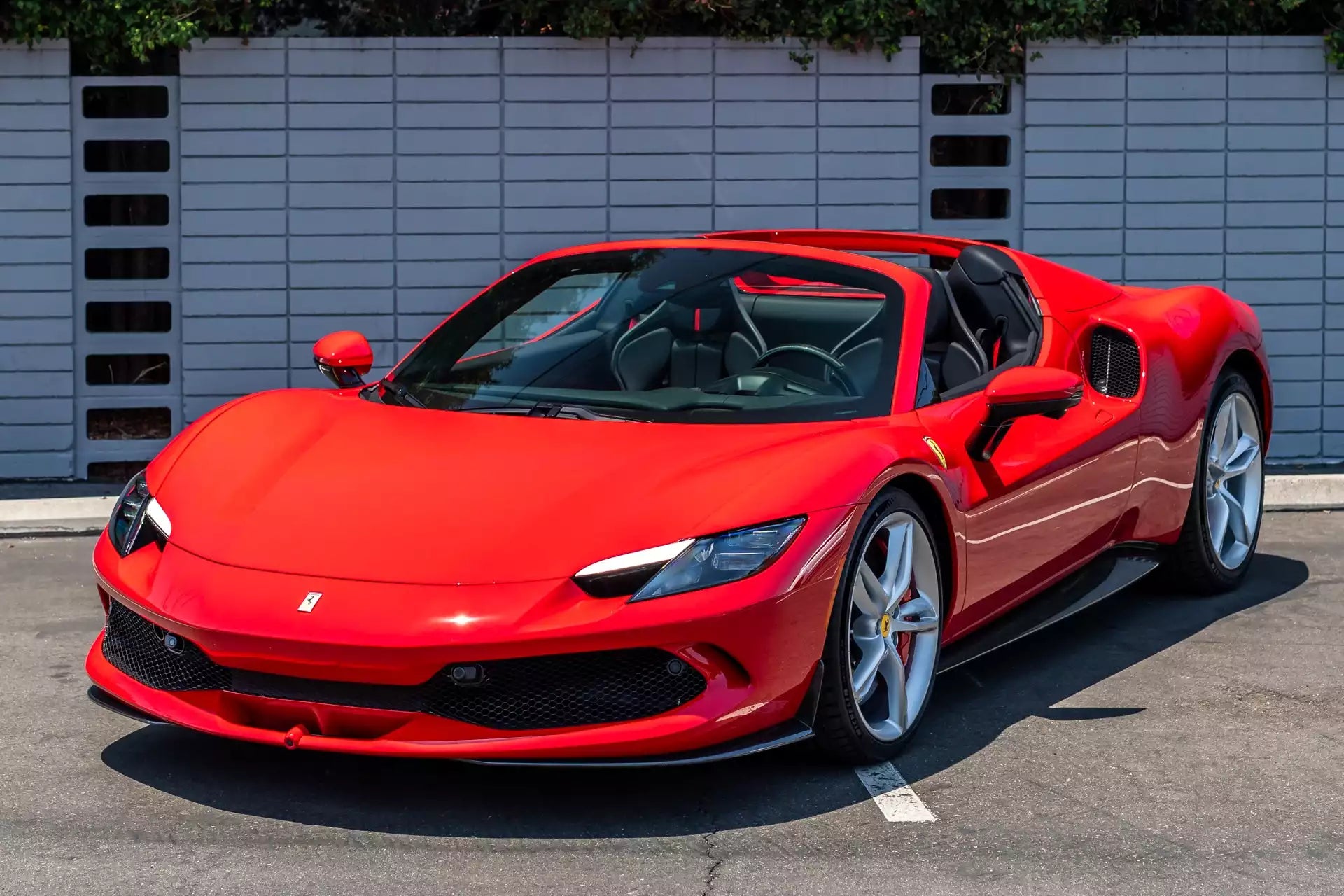 Red sports car parked on a street with a white wall in the background
