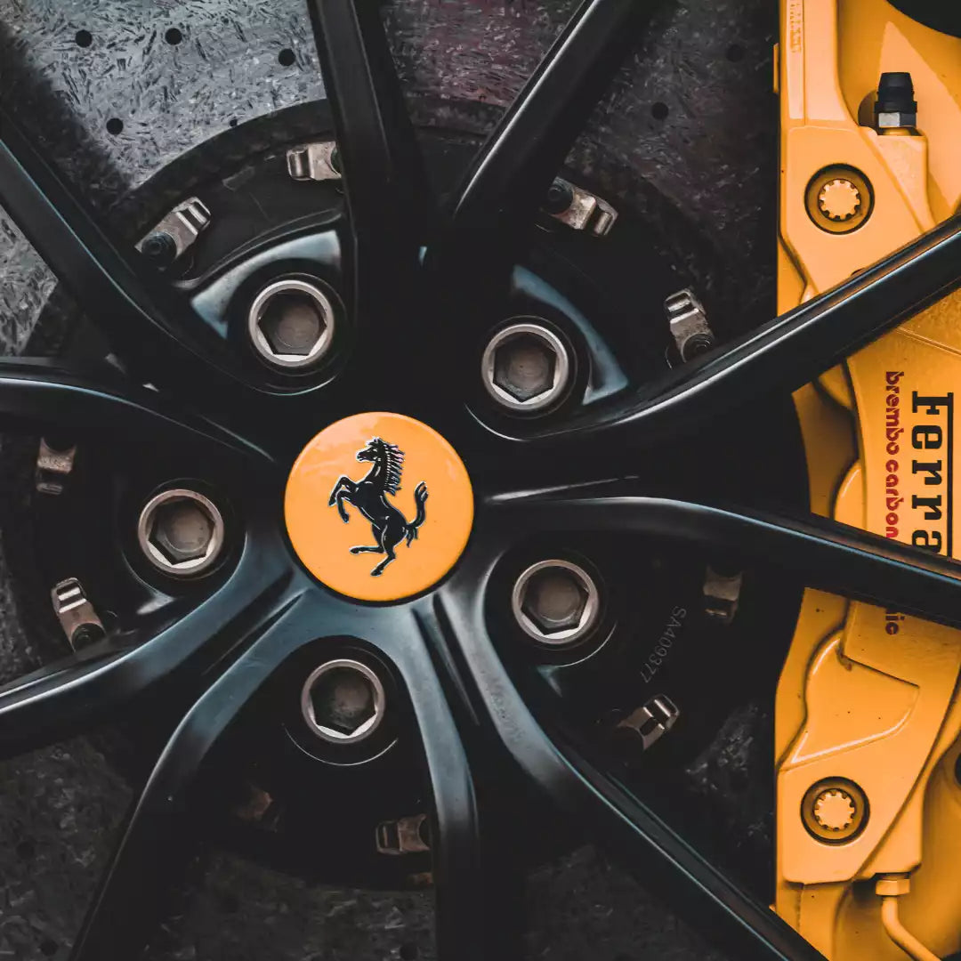 Close-up of a black Ferrari wheel with a bright orange center cap featuring the black prancing horse logo, alongside a yellow brake caliper with visible TERRA branding.