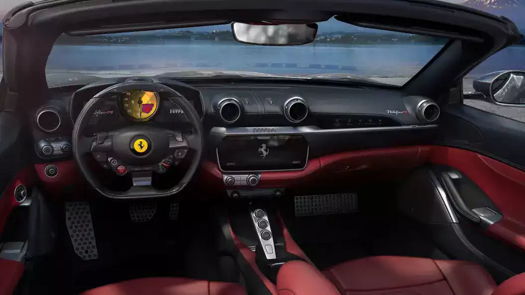 A luxury car interior with a black dashboard and steering wheel, red leather seats and door panels, and visible Ferrari branding on the steering wheel and center console.