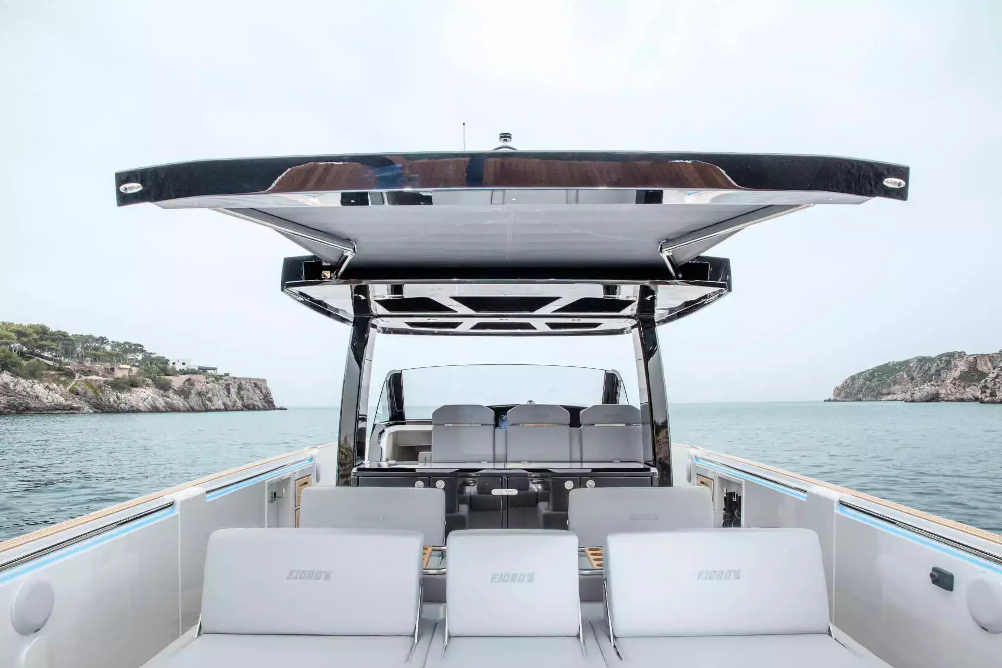Back of a boat with seating area and open roof, overlooking water and coastline.