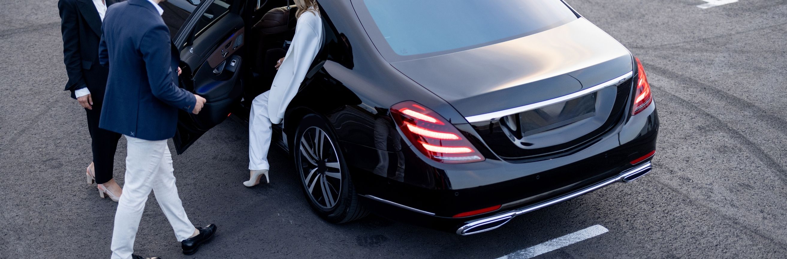 Two people getting into a black Mercedes-Benz car on a road.