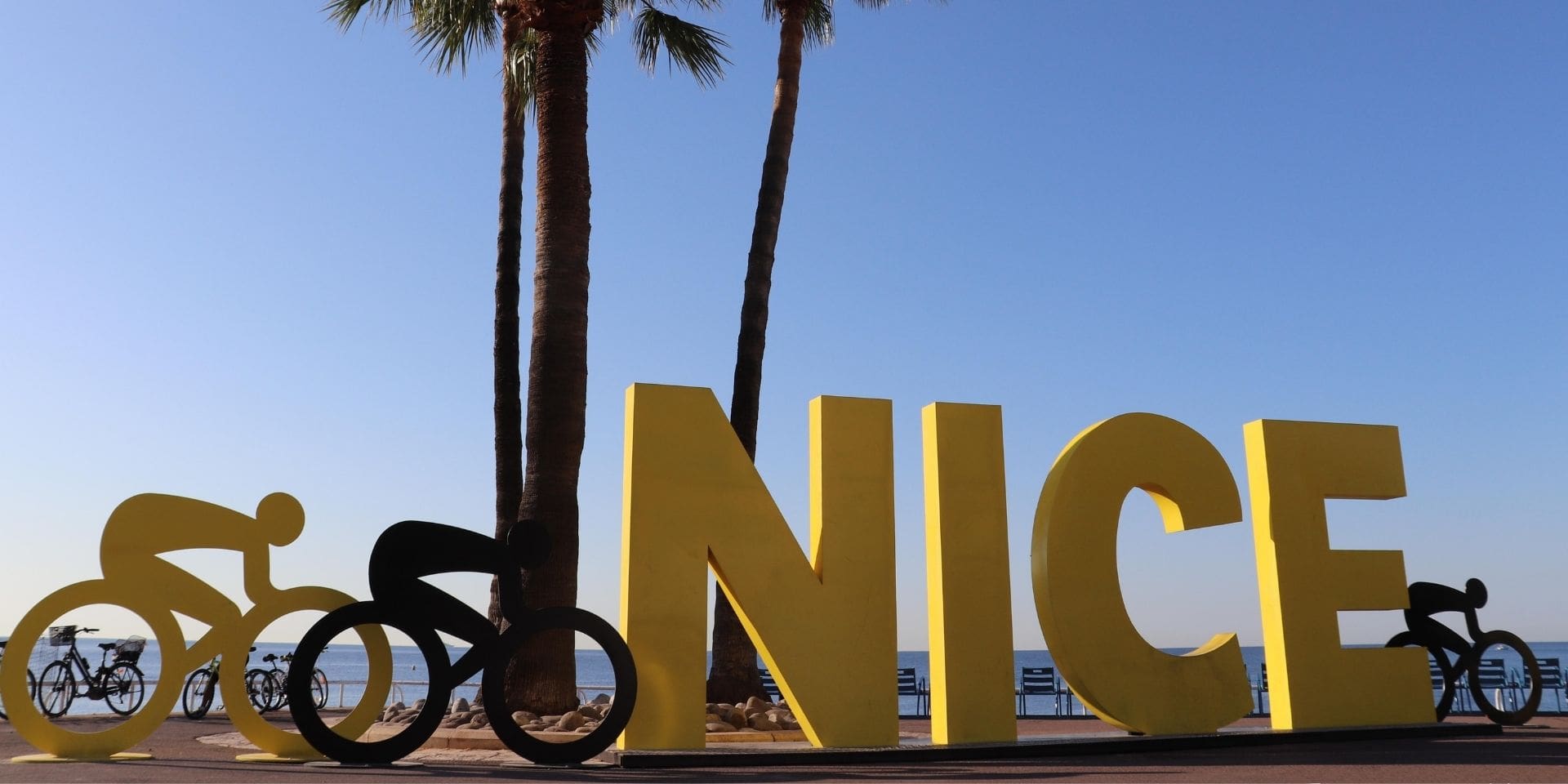 Large yellow letters spelling 'NICE' with bicycle and palm tree sculptures against a blue sky.