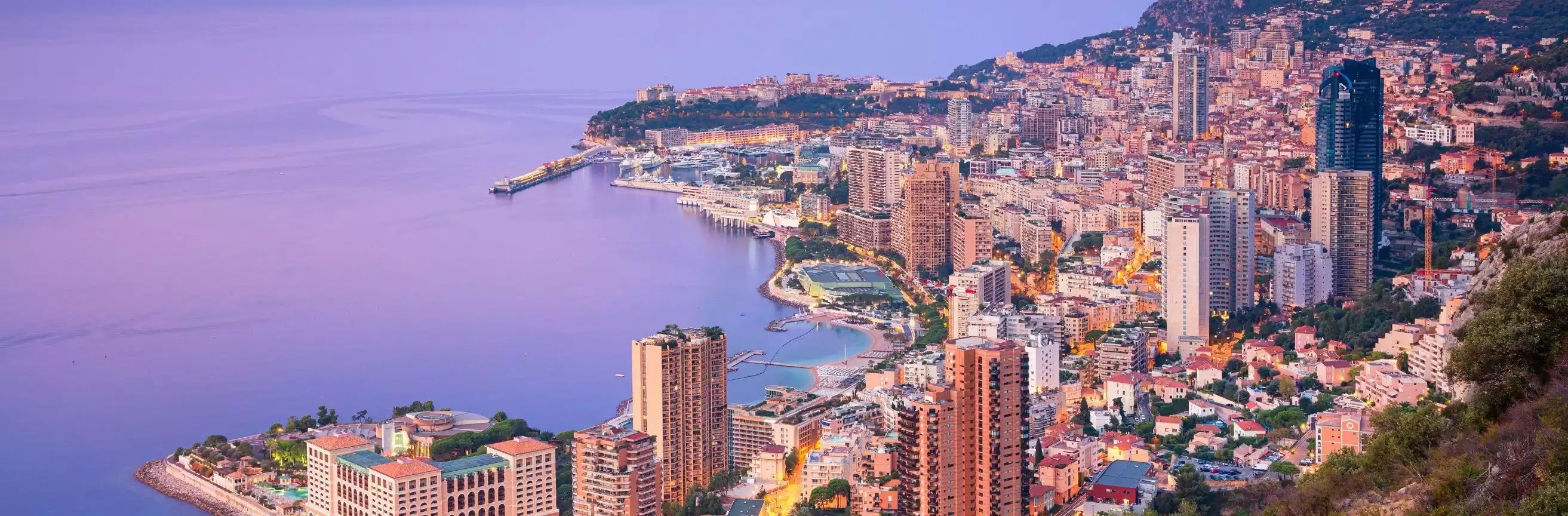 Cityscape of Monaco with buildings and coastline at sunset.