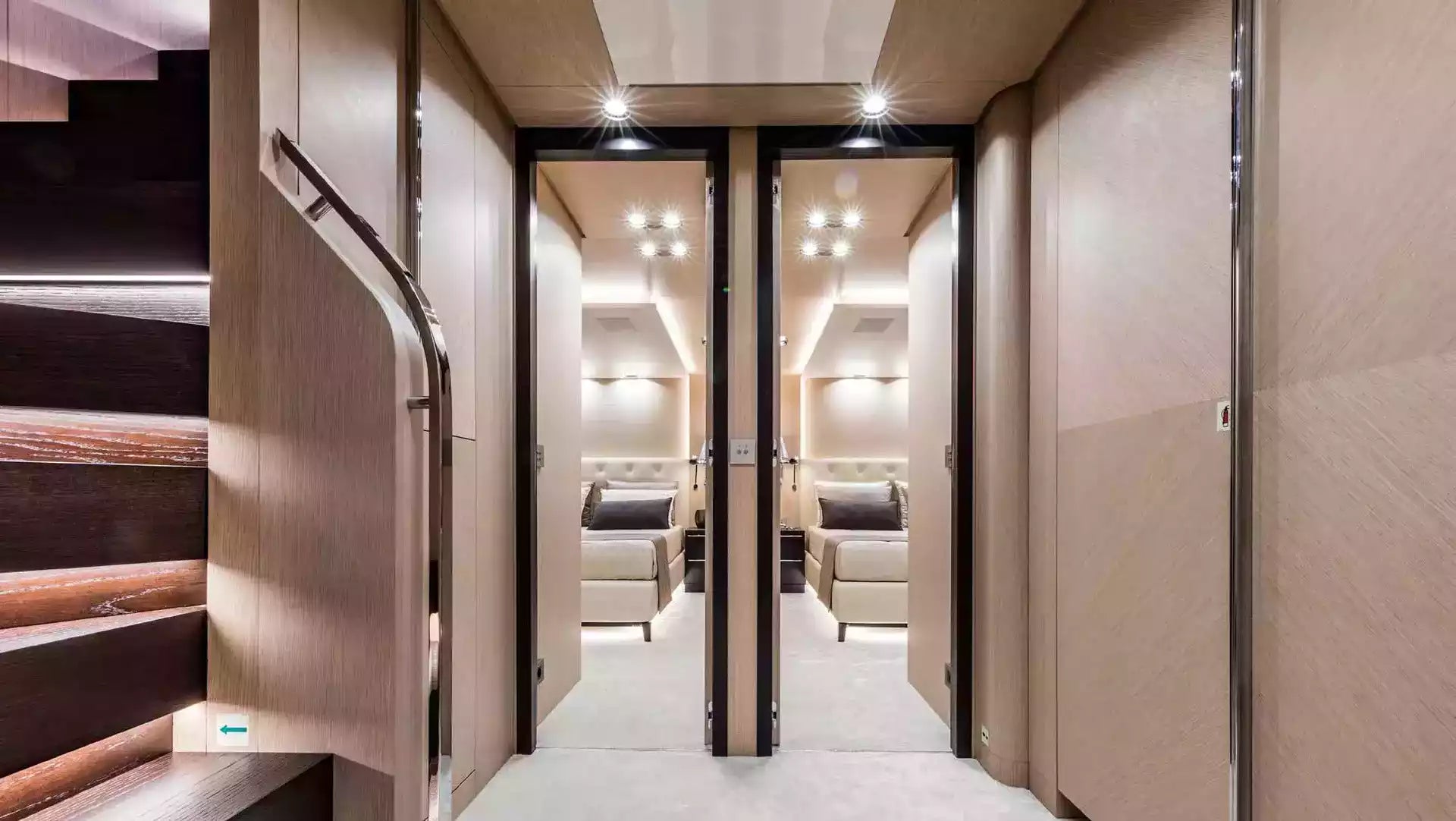 A luxury interior hallway with light wood walls and doors, leading to two bedrooms with beige beds and warm recessed lighting. A dark wood staircase with integrated lighting is visible on the left.