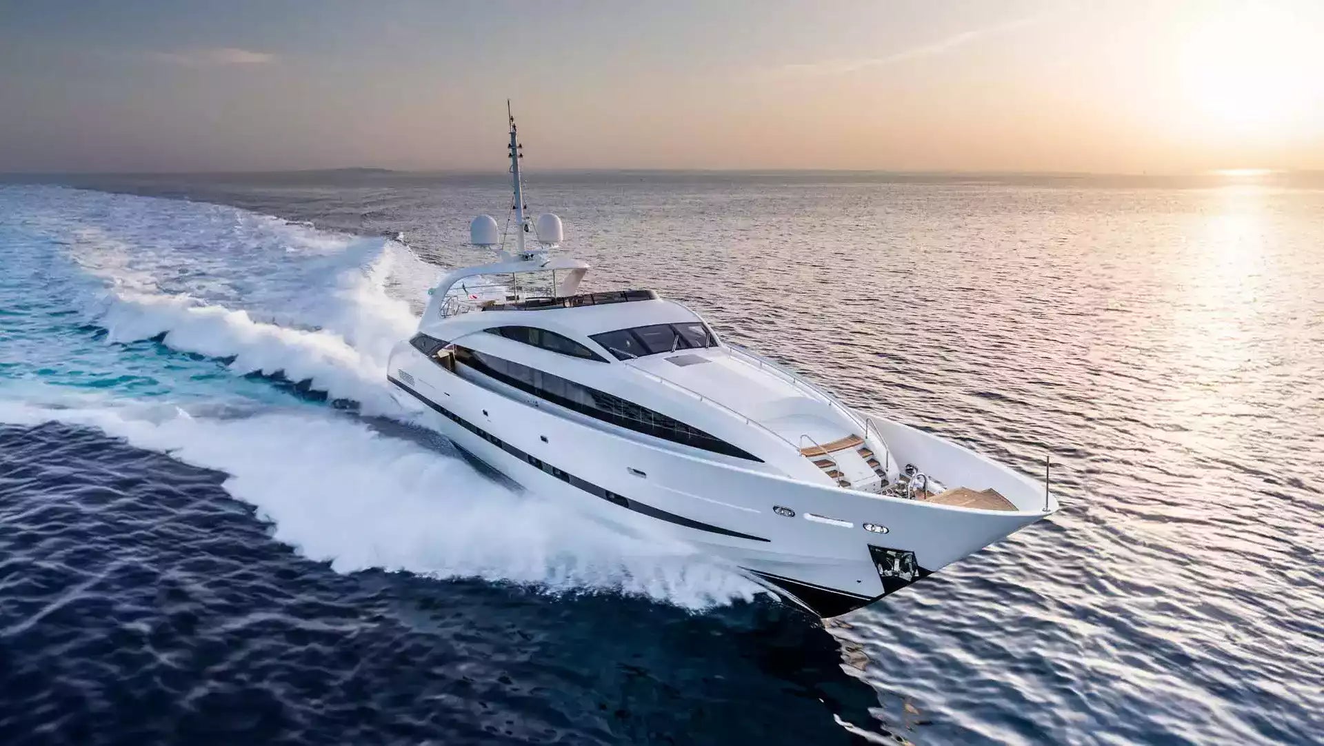 A luxury white motor yacht cutting through deep blue ocean water at sunset, leaving a large white wake behind it.