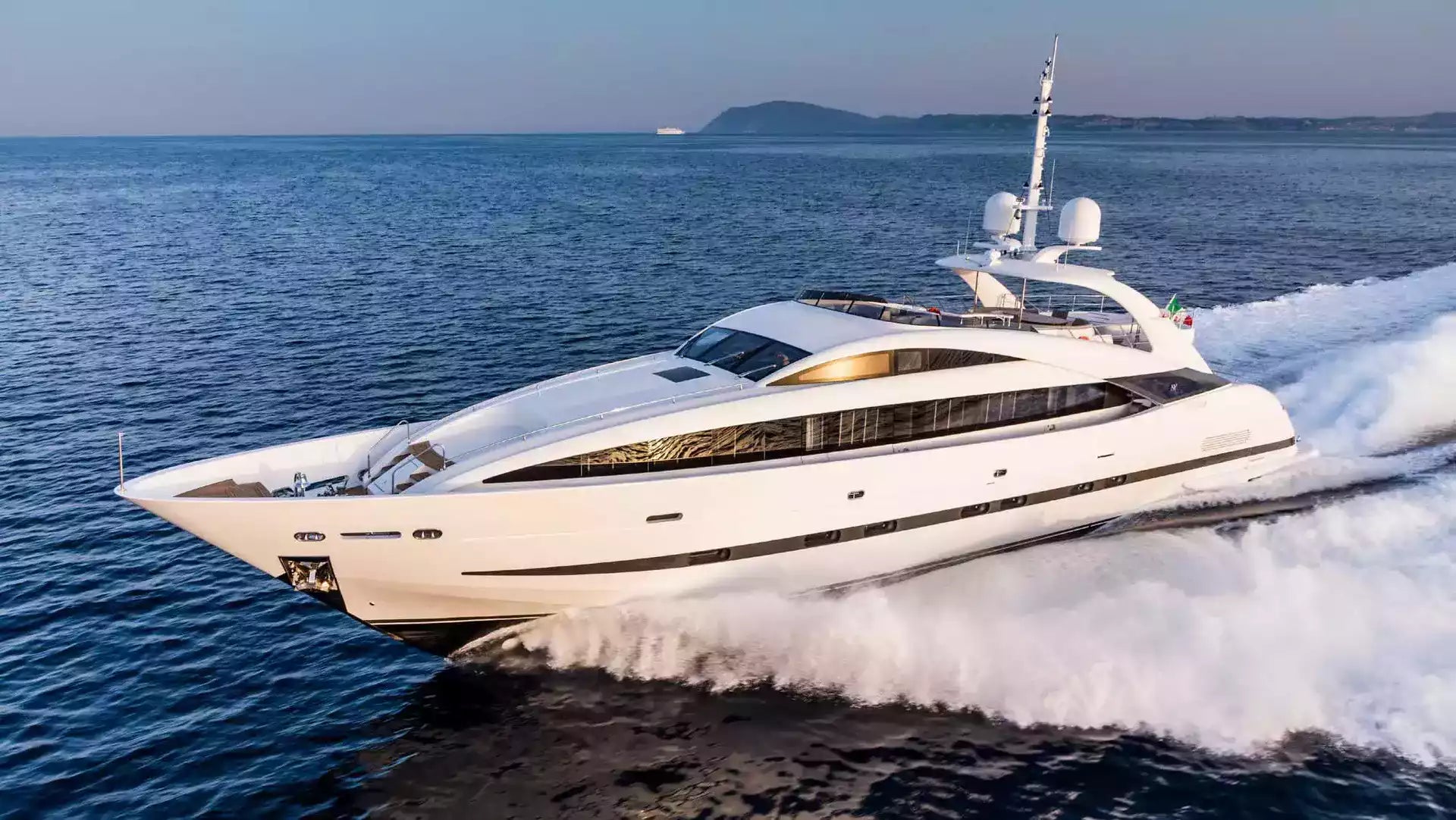 A luxury white motor yacht speeds across deep blue ocean water, creating a large white wake behind it under a clear sky.