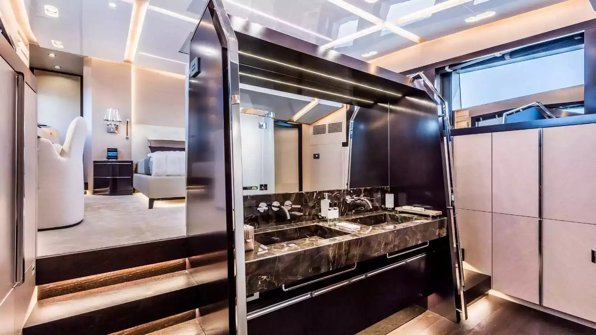 Luxury yacht bathroom featuring a double vanity with a dark marble countertop, integrated sinks, a large overhead mirror with LED lighting, and sleek dark cabinetry.