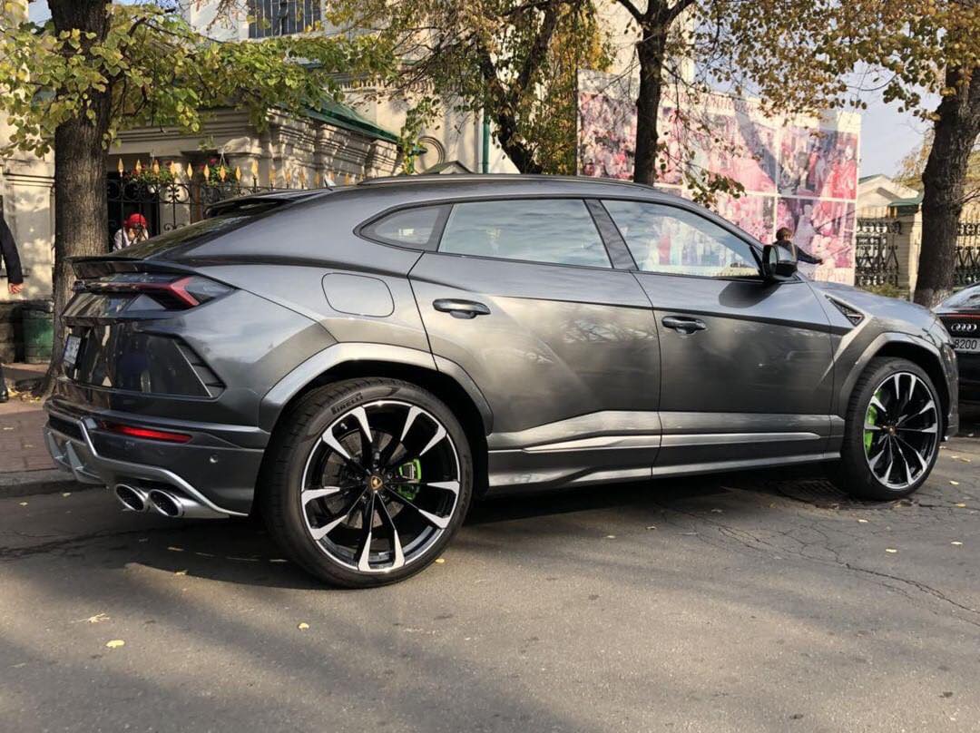 Gray Lamborghini SUV parked on a street with trees and buildings in the background