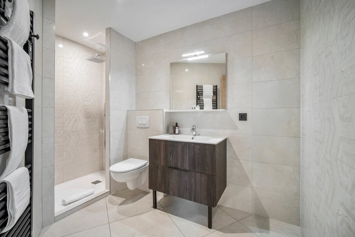 Modern bathroom vanity with a dark wood cabinet, white sink countertop, and a large mirror, shown in a tiled bathroom with a walk-in shower and heated towel rails.