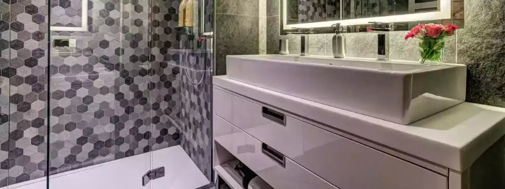 Modern bathroom vanity with a white rectangular vessel sink, white floating cabinet, patterned gray hexagonal tile wall, and a glass shower enclosure.
