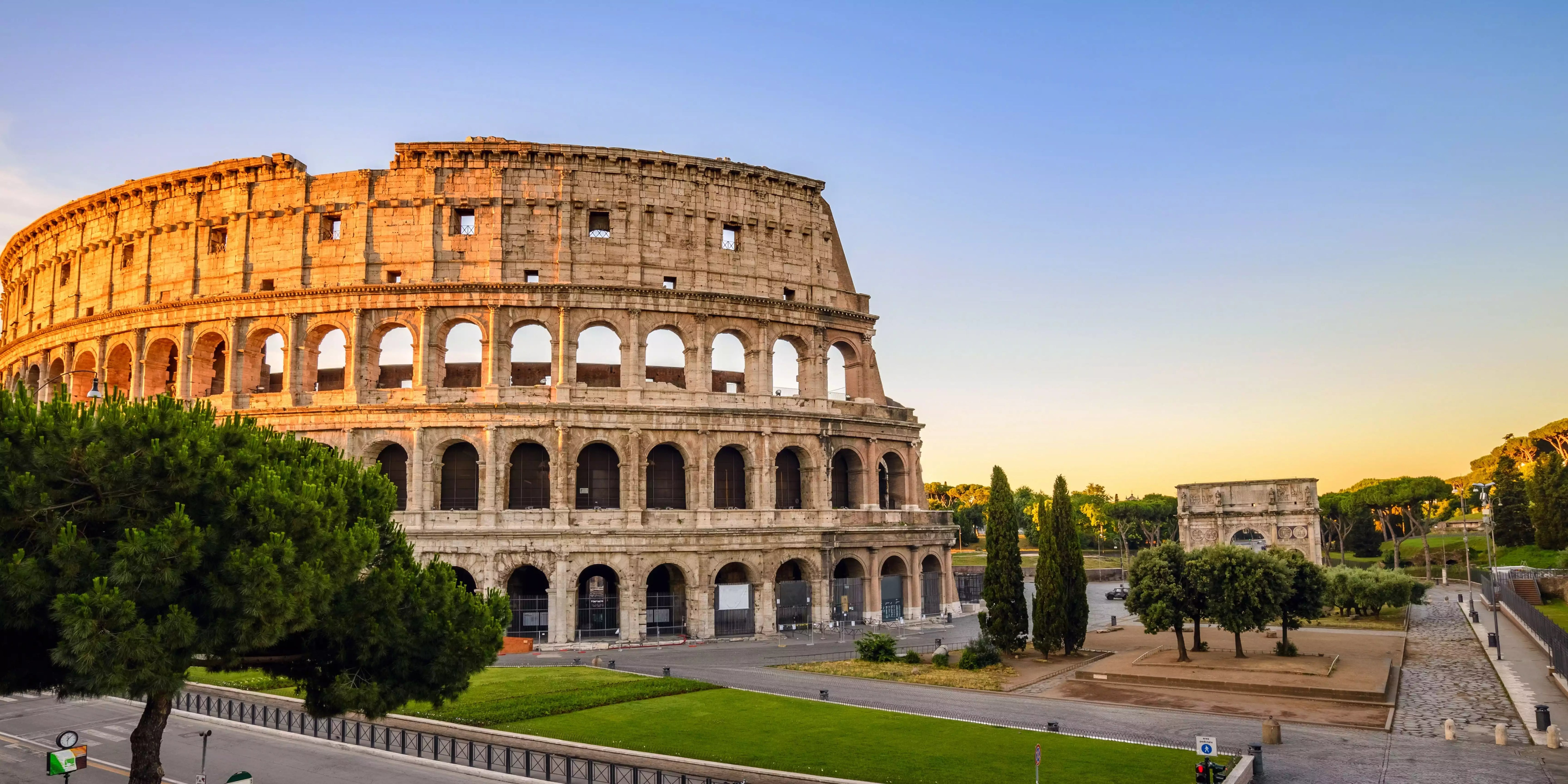 The Colosseum in Rome during sunset with trees and a clear sky.