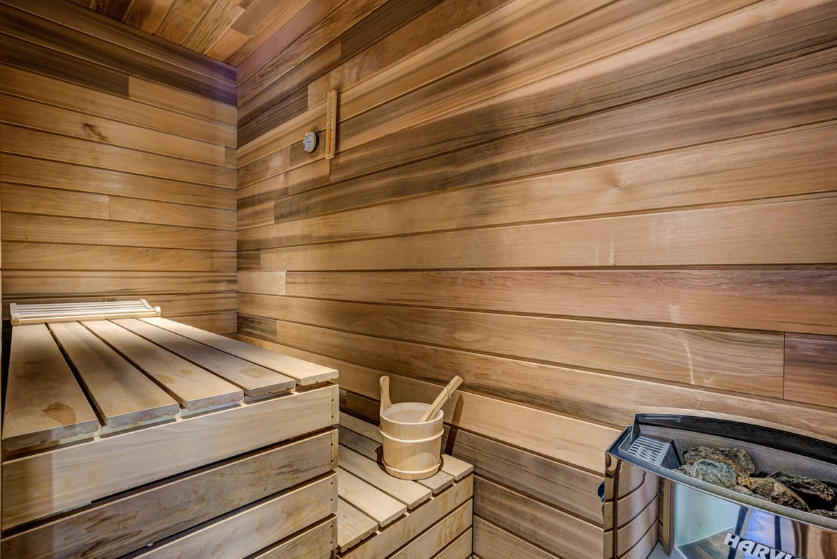 A traditional wooden sauna interior with wooden walls and benches, a small wooden bucket with a wooden spoon, and a steam generator on the right side.