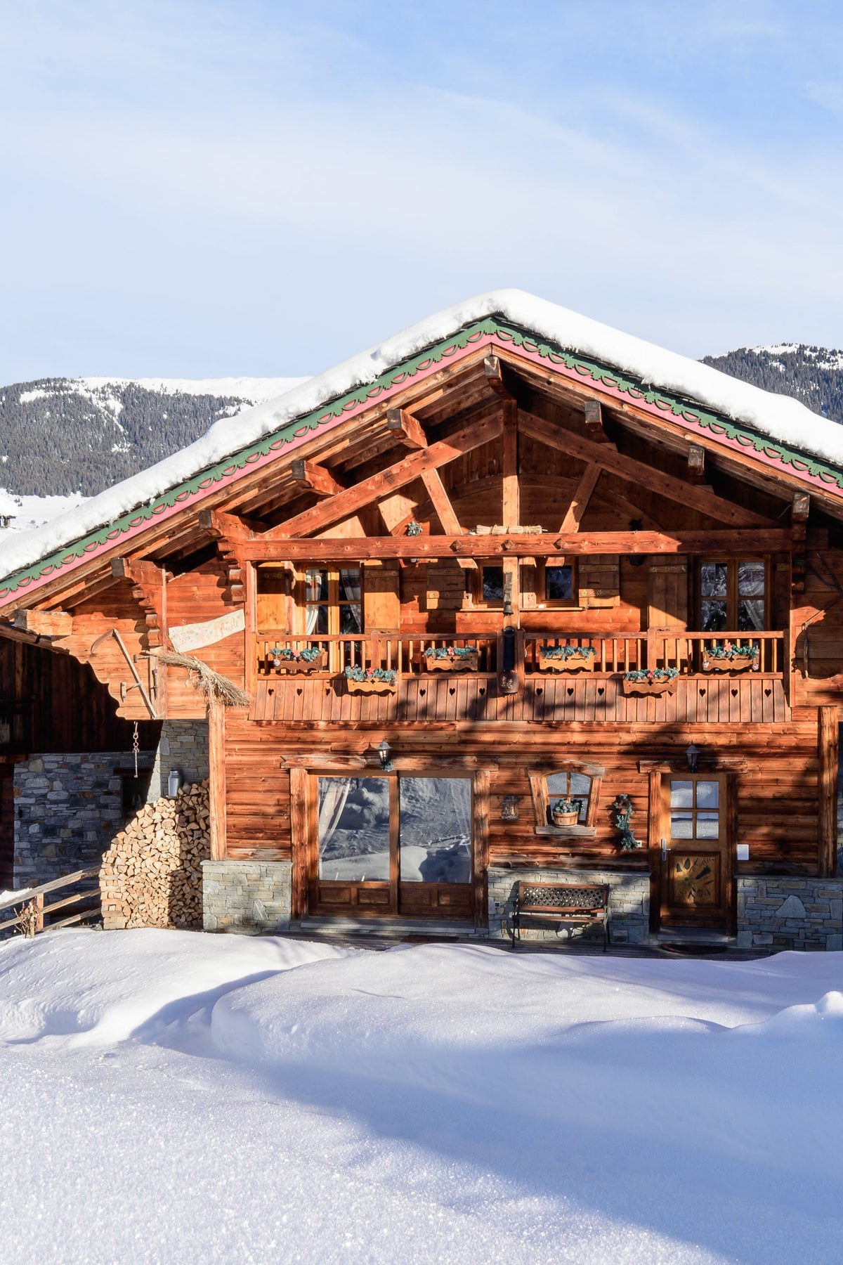 A large traditional alpine chalet with snow-covered roofs and wooden exterior walls, set in a snowy mountain landscape under a blue sky.