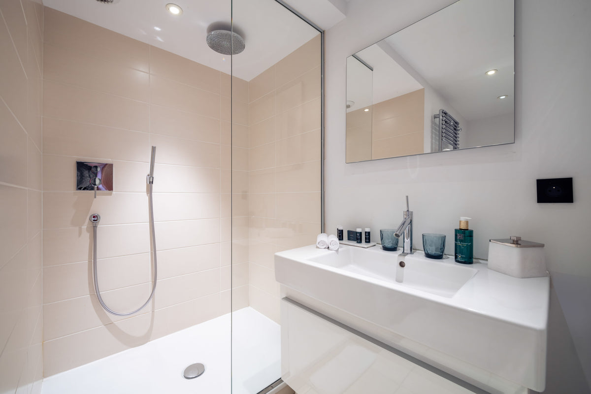 Modern bathroom interior with a walk-in shower enclosure, white floating vanity, chrome faucet, beige tiled walls, and a large rectangular mirror.