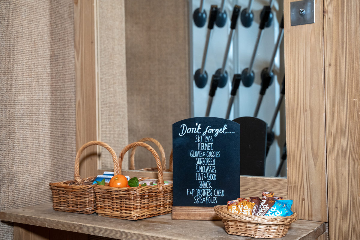 A rustic wooden door entryway with a small chalkboard sign reading 'Don't forget...' and baskets of snacks and items inside.