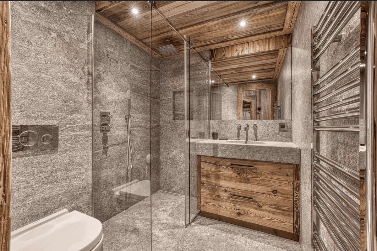 A luxury modern bathroom featuring a large walk-in glass shower enclosure with stone walls, a rustic wood vanity with a stone countertop, and a wood ceiling.
