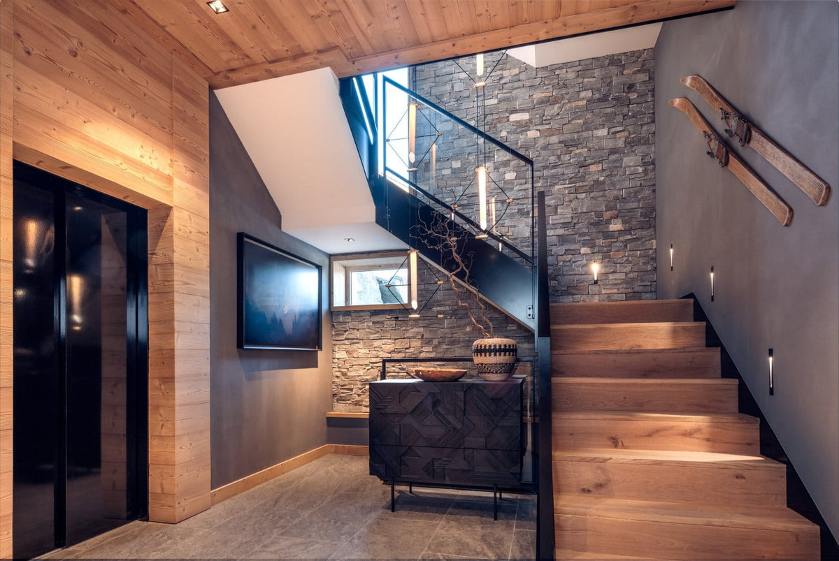 A modern interior staircase with light wood steps, a stone wall, black railings, and ski decor mounted on the wall.