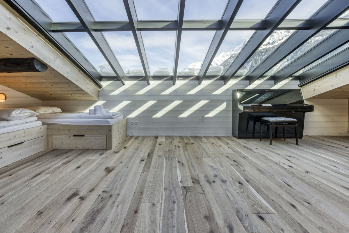 A luxury attic bedroom featuring light wood flooring, a built-in bed, a black grand piano, and a large glass skylight looking out to snowy mountains.