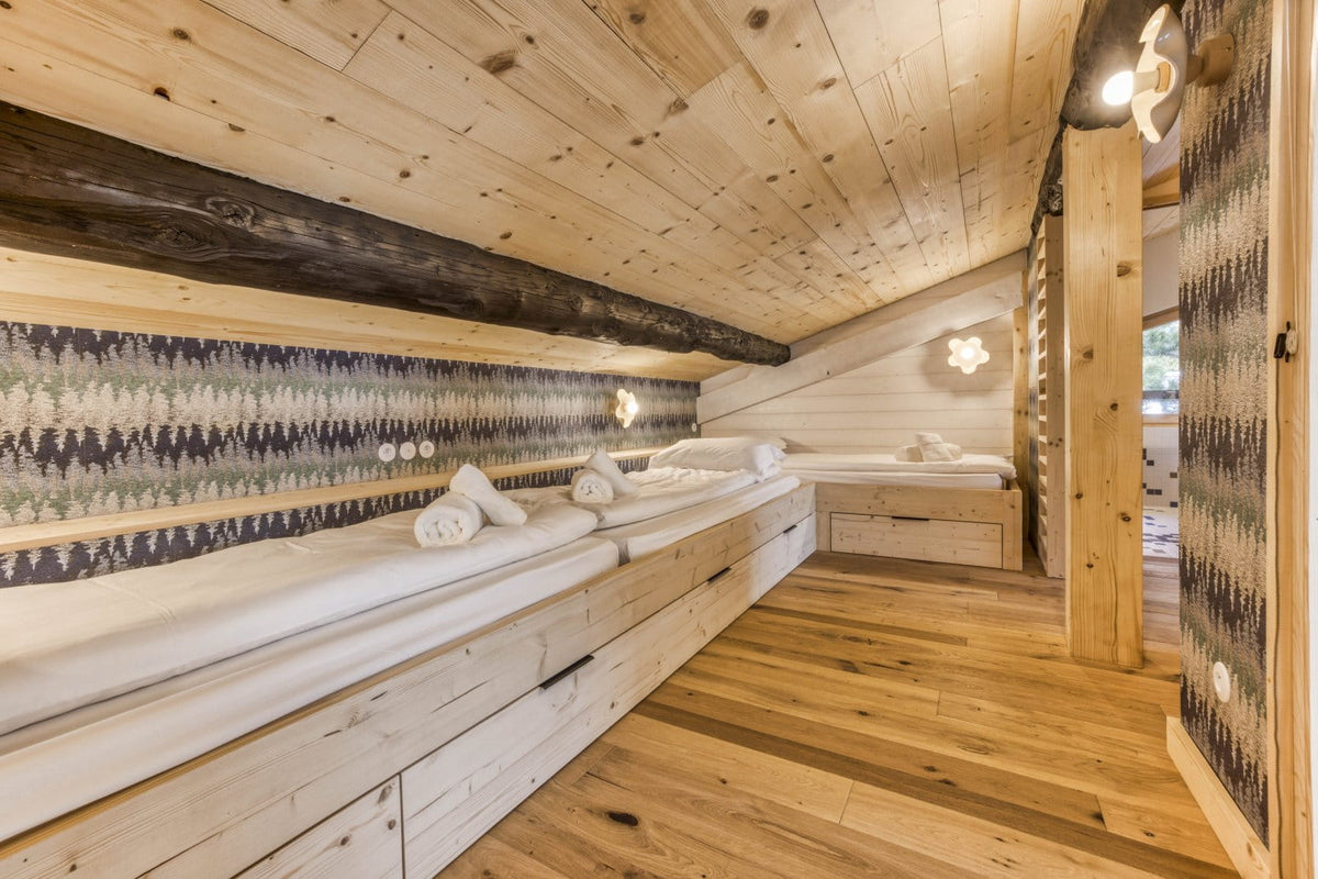 A rustic wooden sauna room with long built-in wooden benches, white towels, patterned wallpaper, and warm wood paneling on the ceiling and floor.