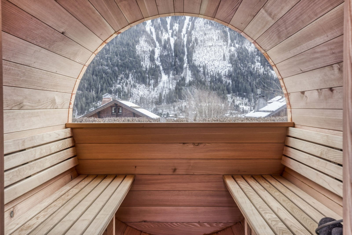 A wooden sauna interior with tiered benches and a large arched window overlooking a snowy mountain landscape.