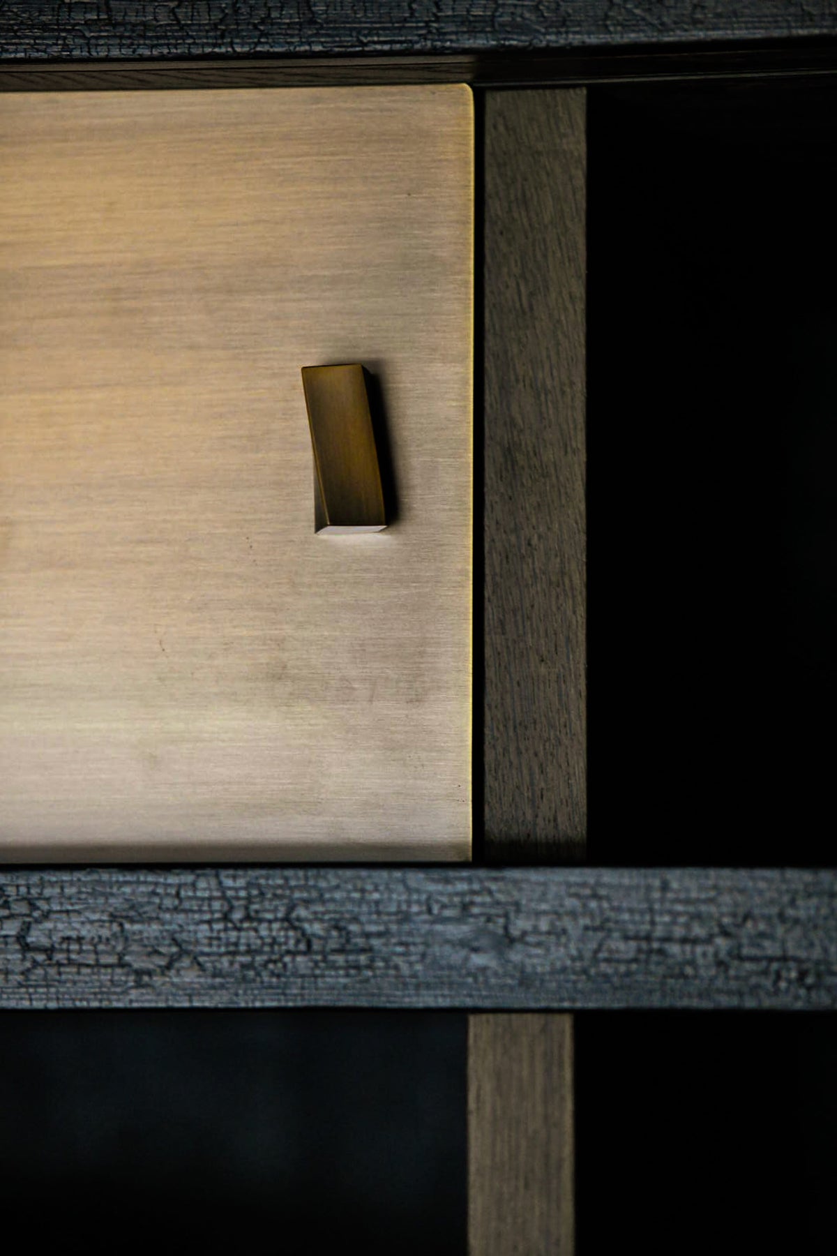 Close-up of a wooden cabinet or drawer front with a small rectangular brass pull handle, set against a dark wood frame.