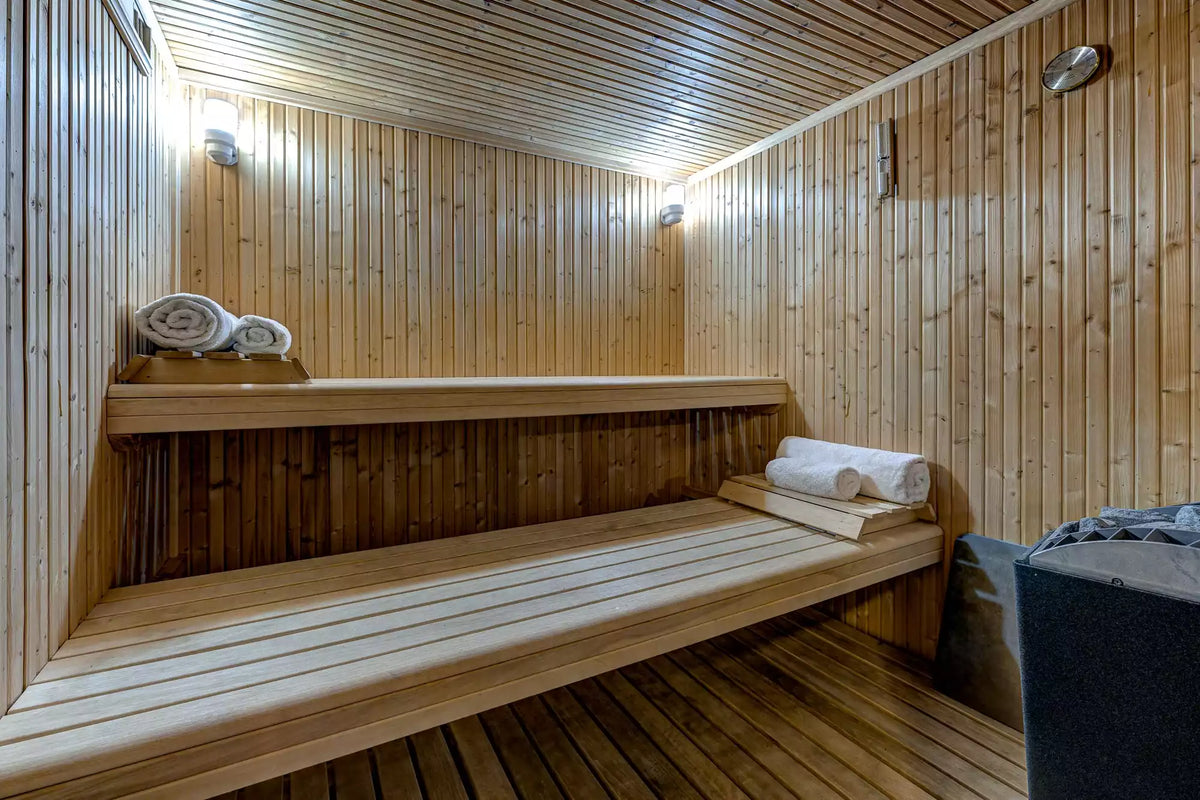 A wooden sauna room with built-in benches, wood-paneled walls and ceiling, rolled white towels, and wall-mounted lights.