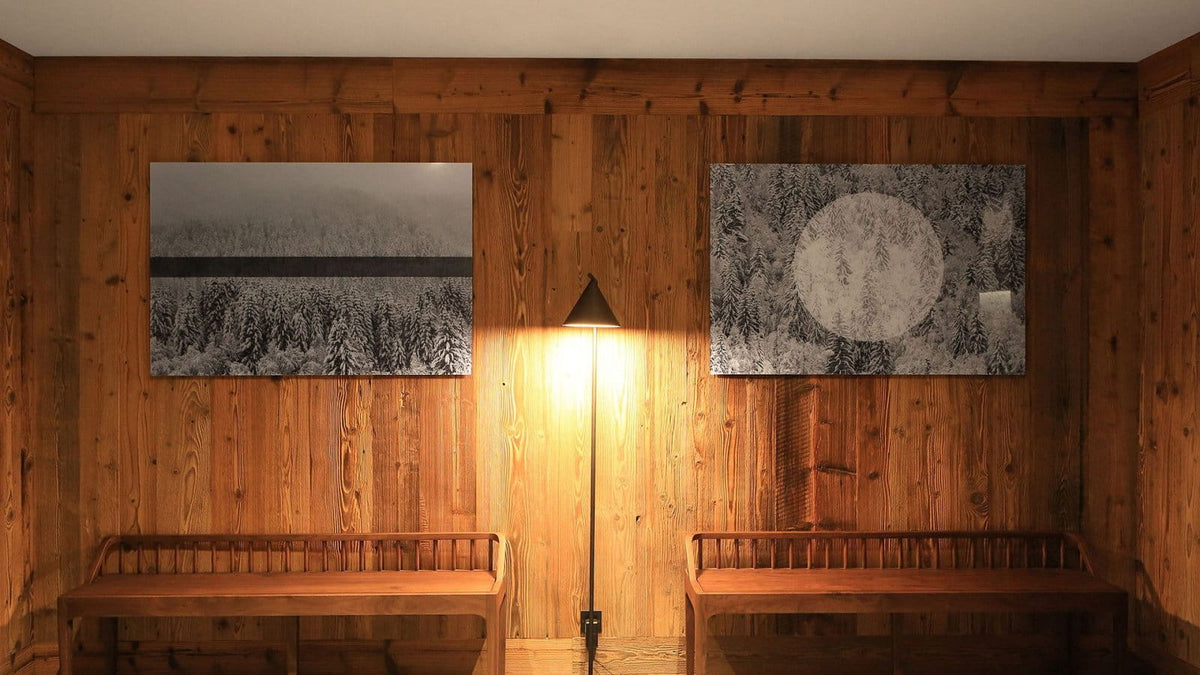 A warm, rustic interior with wood-paneled walls, two framed landscape art prints, a floor lamp, and wooden benches.