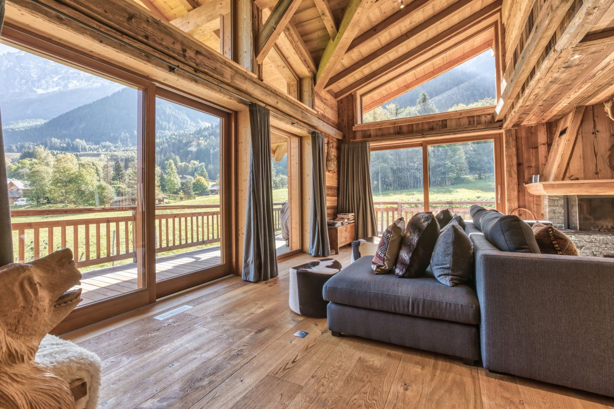 A modern gray fabric sectional sofa with patterned throw pillows in a rustic wooden chalet living room, featuring large windows with mountain views.