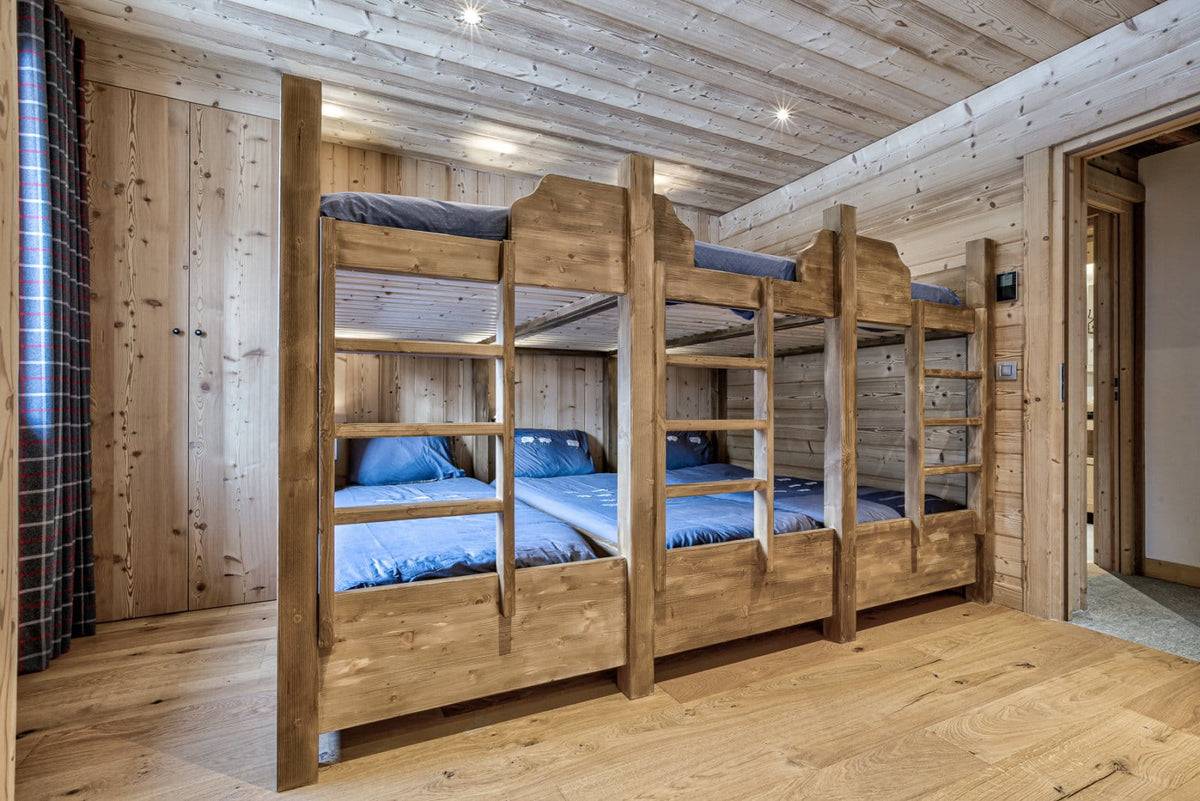 A rustic wooden bunk bed set with three single beds, featuring blue bedding, set in a cozy wood-paneled bedroom.
