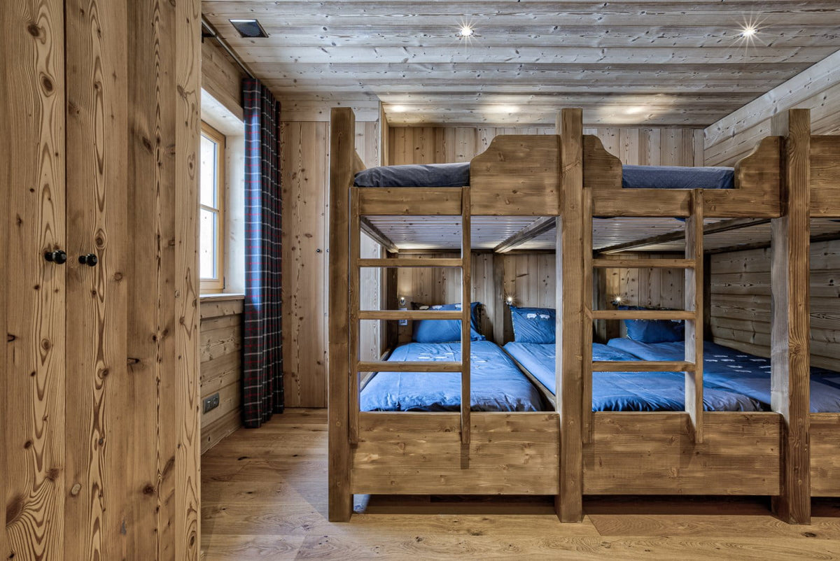A rustic wooden cabin bedroom featuring three wooden bunk beds with blue bedding, set against light wood paneled walls and ceiling.