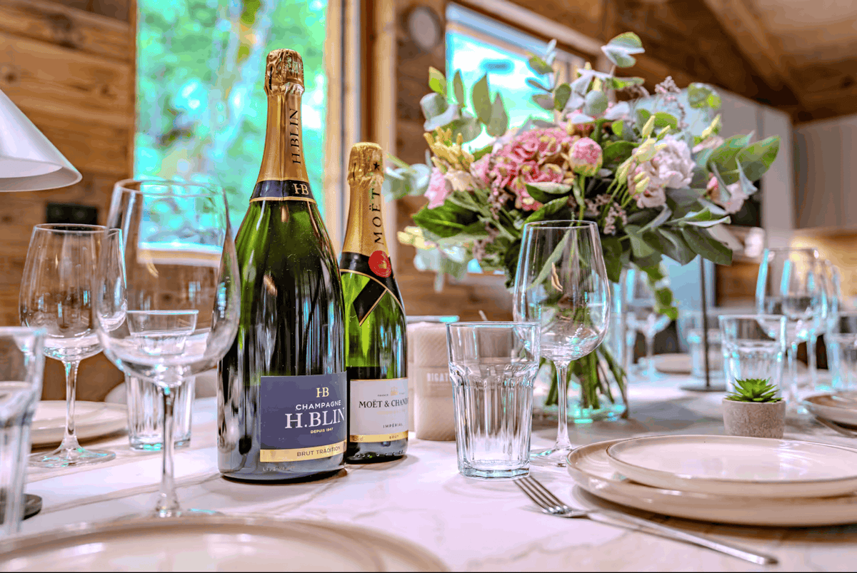 Two bottles of champagne and moétte on a beautifully set dining table with wine glasses, plates, and a floral centerpiece in a rustic wooden room.