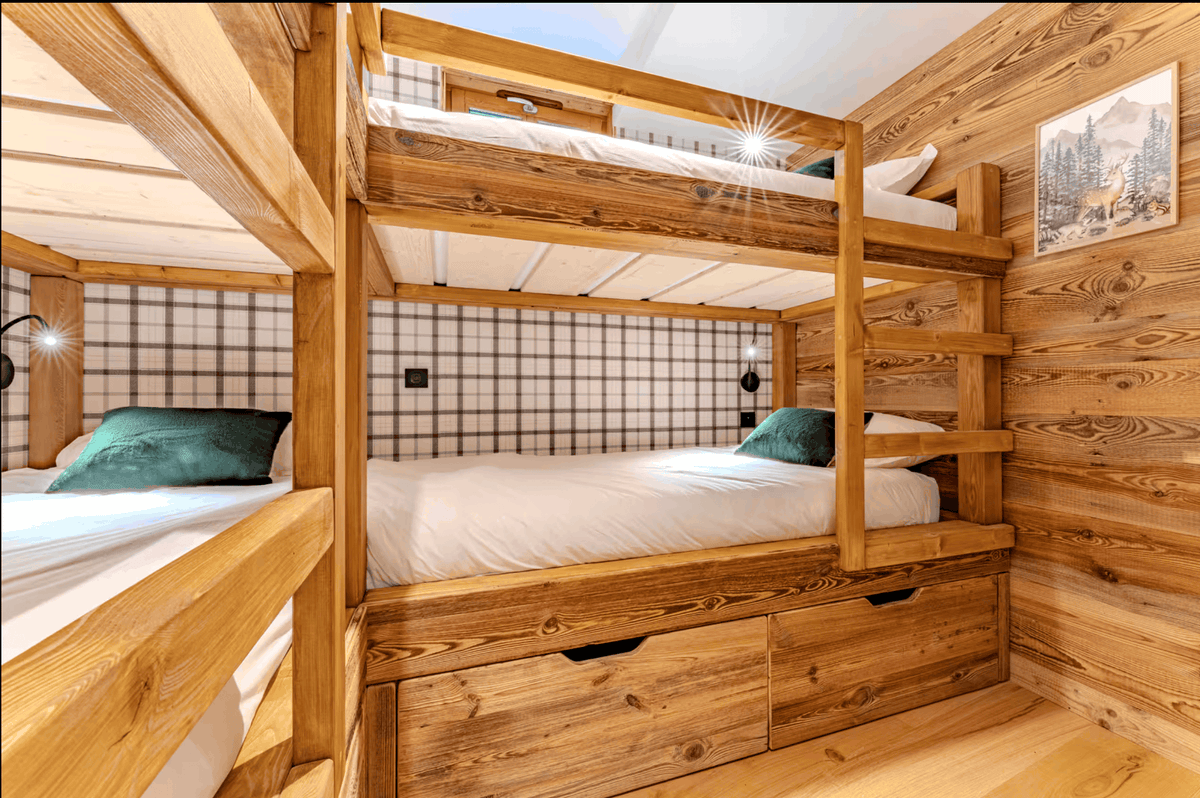 A rustic wooden bunk bed with three single beds, featuring a natural wood frame, built-in storage drawers, and a plaid headboard panel in a cozy cabin-style room.