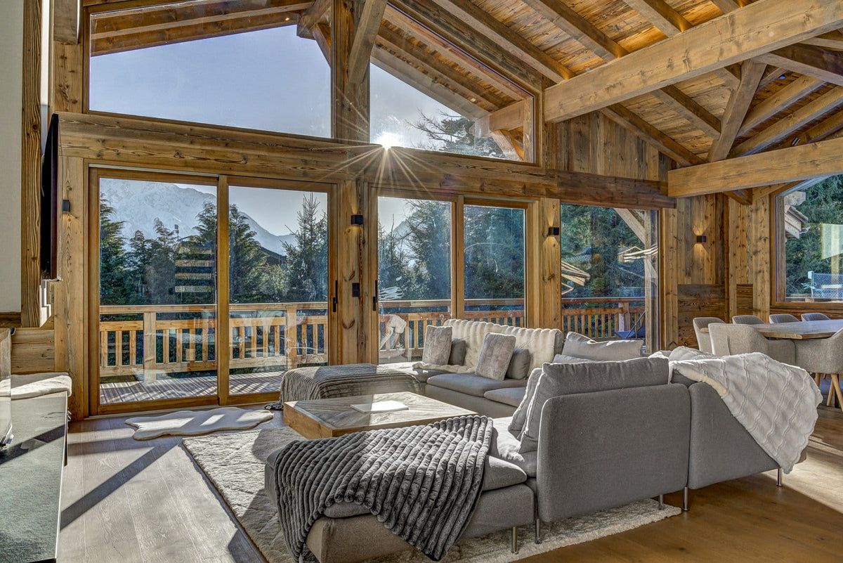 A modern gray sectional sofa in a rustic wooden chalet living room with large windows, mountain views, and a sunburst effect.