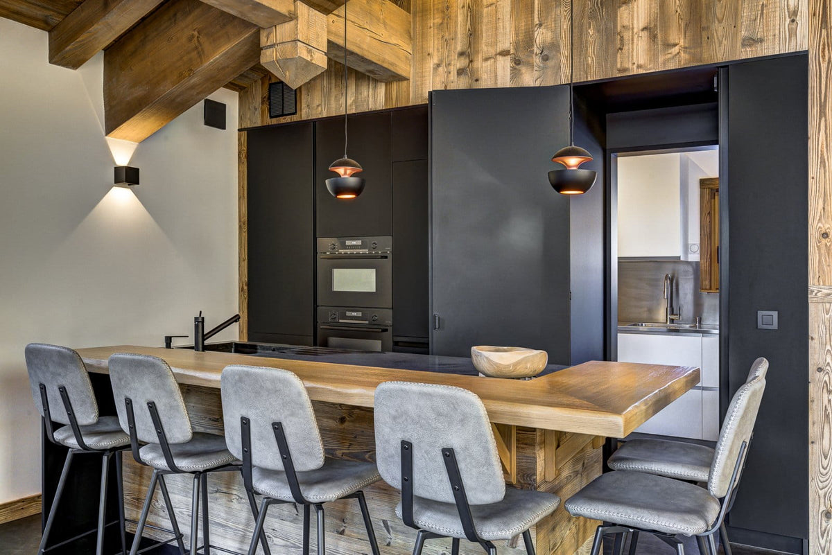 A modern kitchen island with a light wood countertop and bar stools in a rustic, wood-paneled interior.
