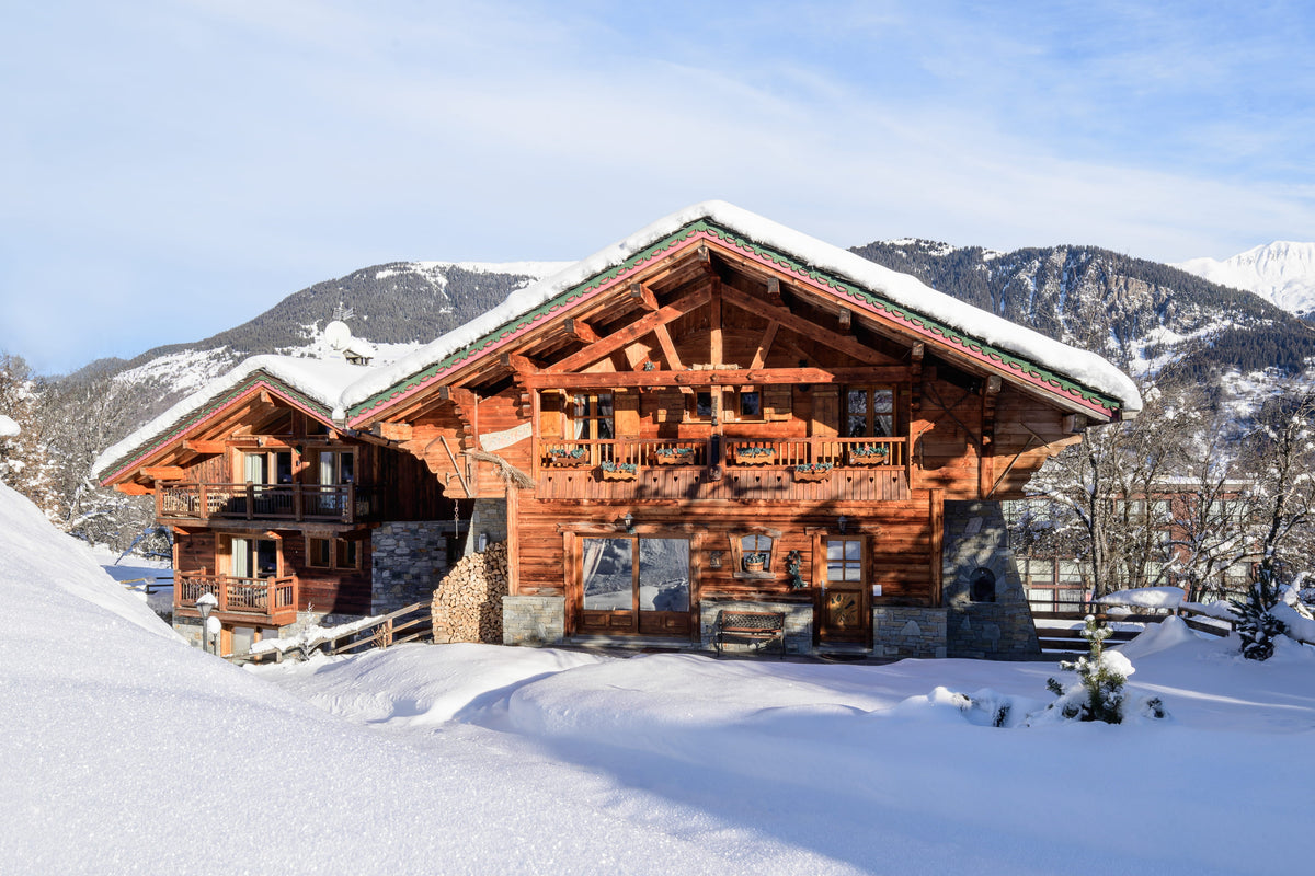 A large alpine chalet with snow-covered roofs and wooden exterior walls, set in a snowy mountain landscape under a blue sky.