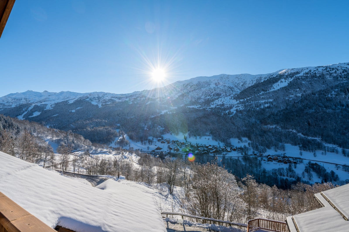 A scenic winter mountain landscape with snow-covered peaks, a bright sun in a clear blue sky, and a valley below with trees and a frozen lake. No product is isolated; the image shows a real outdoor environment.