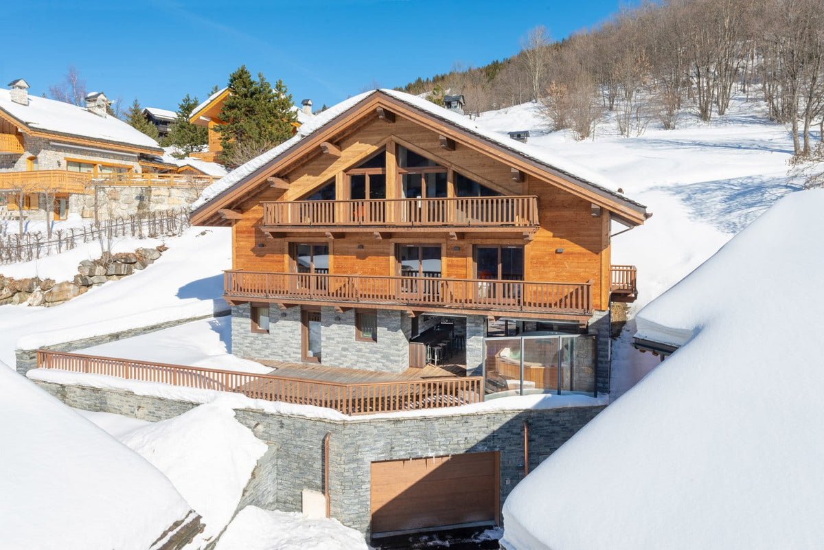 A luxury alpine chalet with warm wood paneling and stone foundations, nestled in a snowy mountain landscape under a clear blue sky.