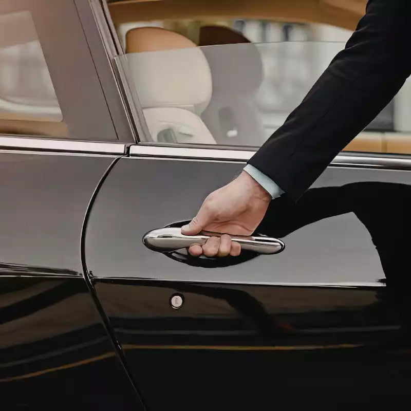 Hand opening a car door, likely from a chauffeur service.