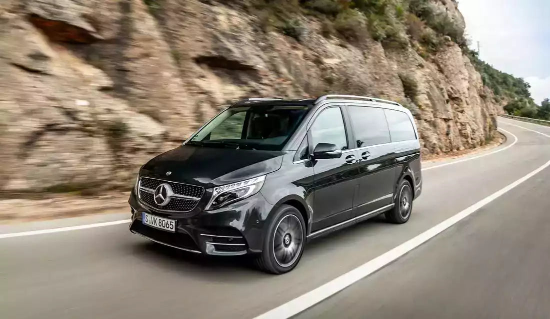 Black Mercedes-Benz van driving on a road with a rocky cliff in the background