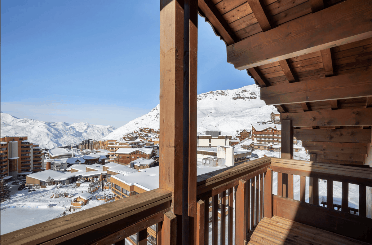 A scenic view from a wooden balcony overlooking a snow-covered mountain village under a clear blue sky.