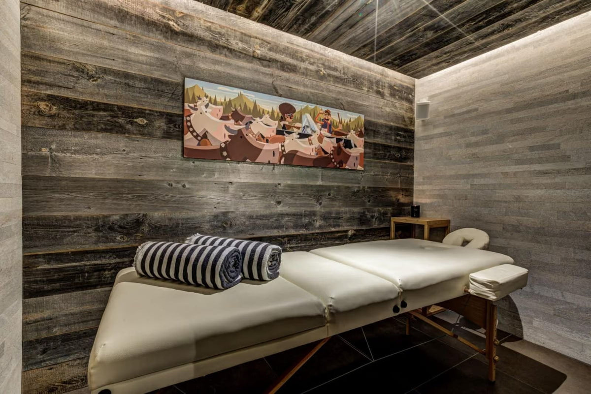 A spa treatment room featuring a padded massage table with a striped towel, set against rustic wood-paneled walls and a matching wood ceiling.