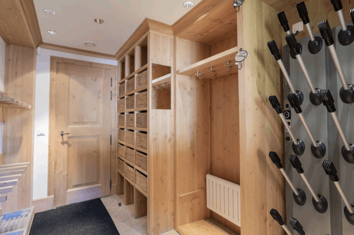 A wooden walk-in closet or gym interior with built-in shelving, woven storage baskets, hanging hooks, a radiator, and a wall-mounted apparatus with black handles and silver metal rods.