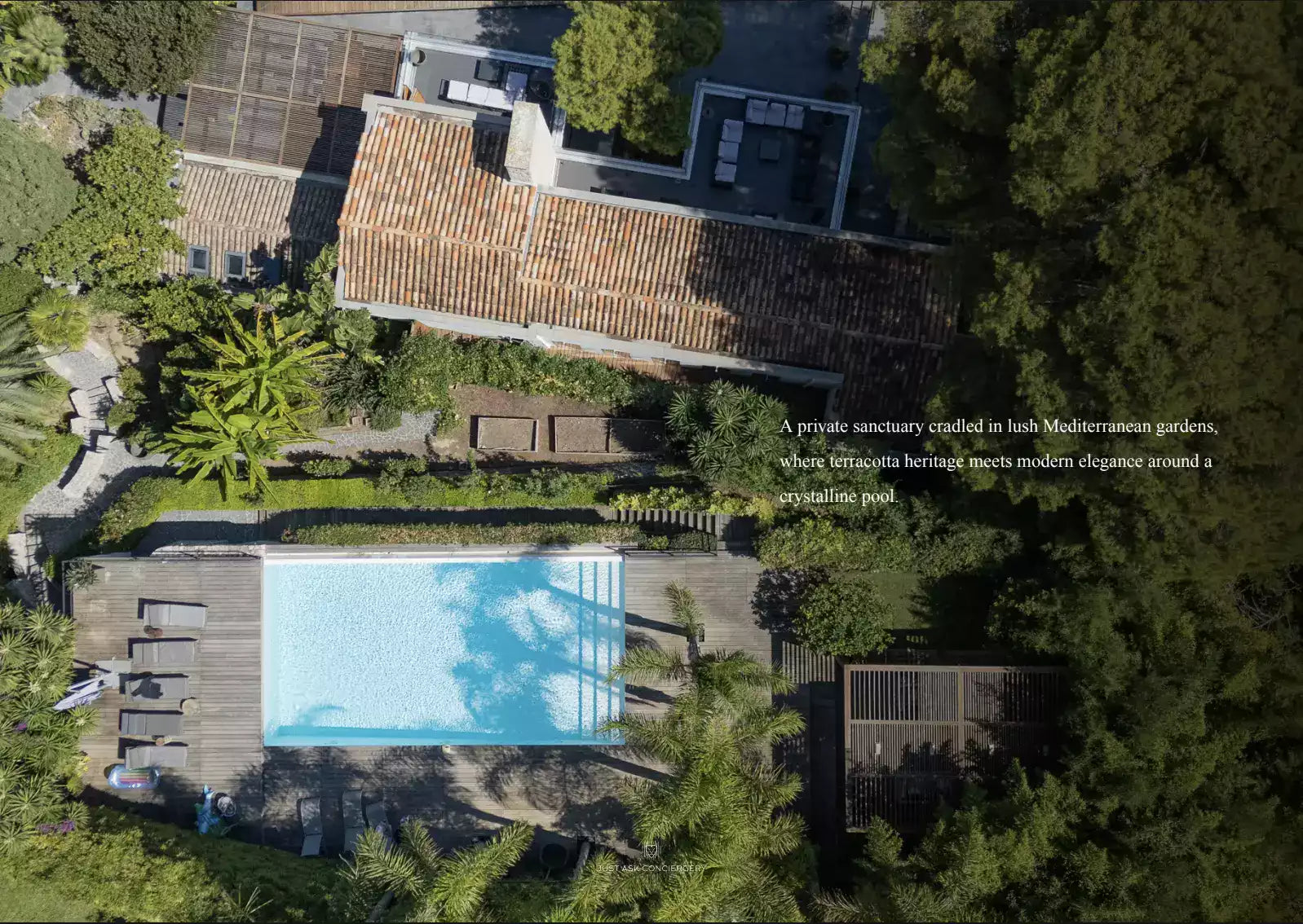 Aerial view of a pool surrounded by lush greenery and a building with a red-tiled roof.